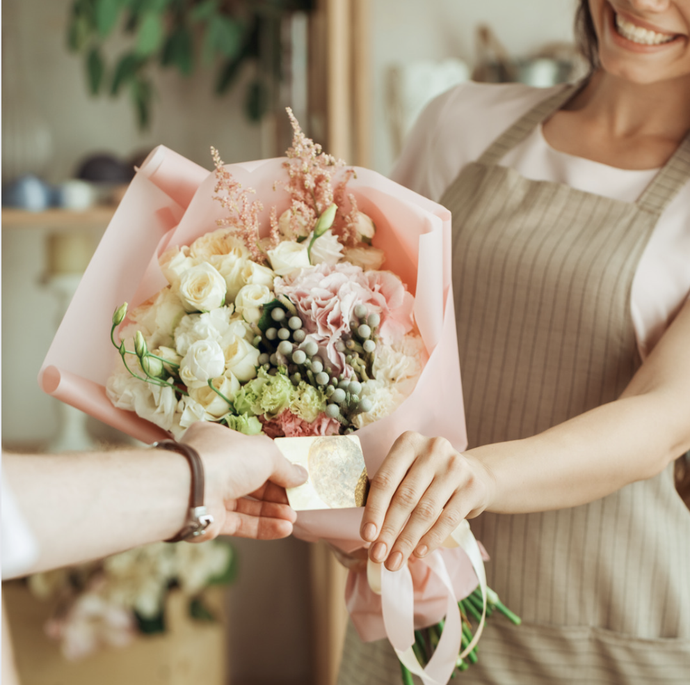 Hand reaching to flower bouquet while florist gives away card