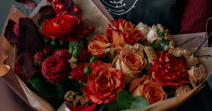 Fall flower bouquet featuring warm autumn blooms in rich orange, yellow, red, and burgundy tones, accented with seasonal greenery.